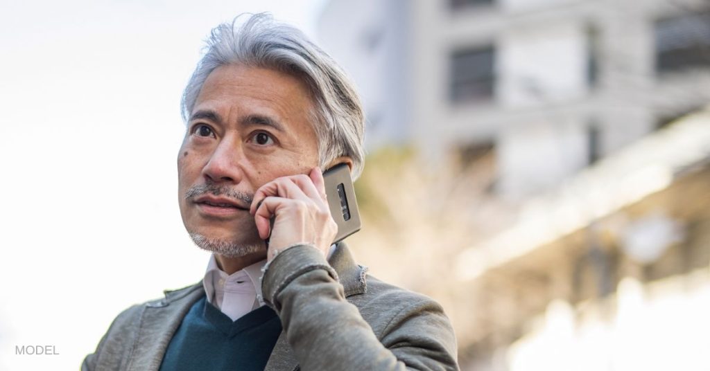 Middle-aged man with a youthful face (model) talking on a cell phone outdoors.